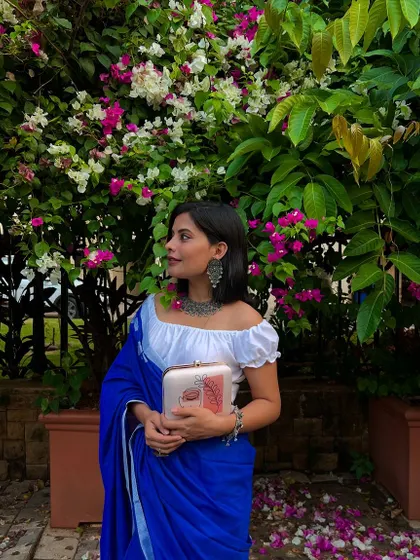 This image perfectly captures a serene and stylish moment. The abstract design on the clutch stands out against the vibrant blue saree, creating a look that is both timeless and contemporary.