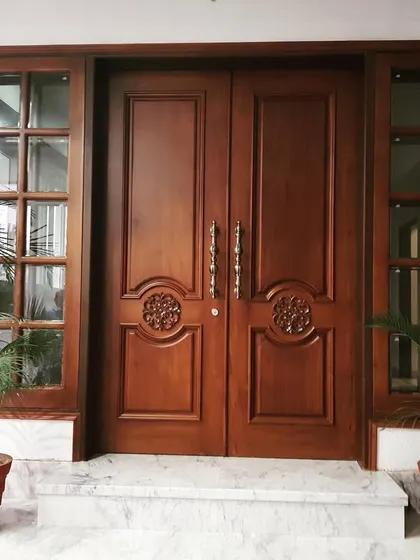 Another example of a classic main entrance. This solid teak wood double door features intricately carved center panels and is flanked by French windows, creating a grand and traditional entryway.