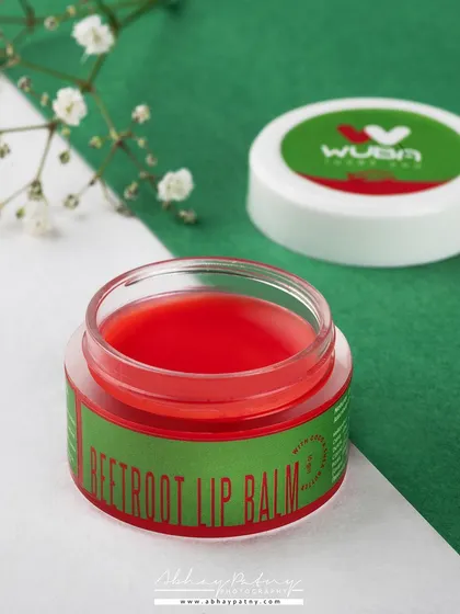 A clean and simple product shot for a beetroot lip balm. The dual-tone background complements the product's packaging, while the open jar shows off the color and texture of the balm inside.