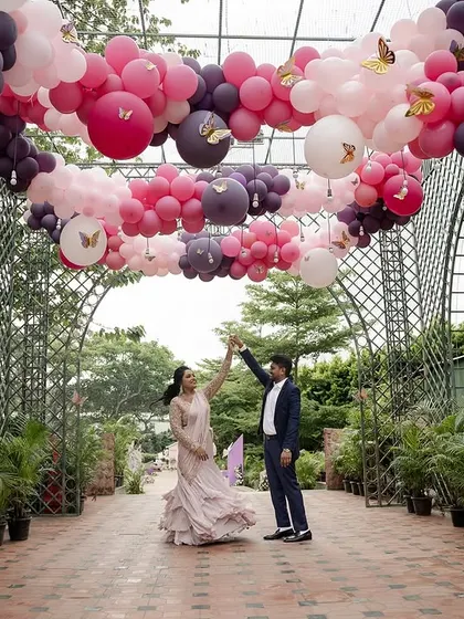 A happy couple dances under a stunning archway of pink and purple balloons, showing how we can create grand, festive moments for any celebration.