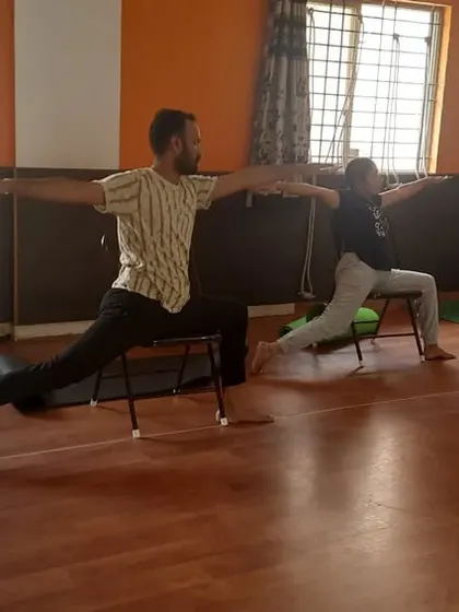 This is another view of our group practicing a modified Warrior Pose with chairs. This setup is particularly helpful for people who find it difficult to put weight on their knees but still want to build leg strength.