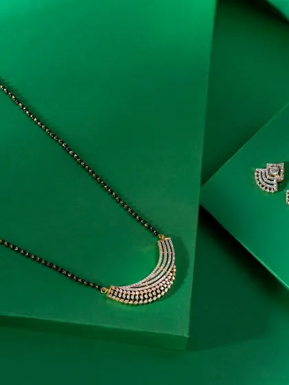 A contemporary mangalsutra set. The necklace features the traditional black beads with a modern, crescent-shaped American Diamond pendant, paired with matching studs.