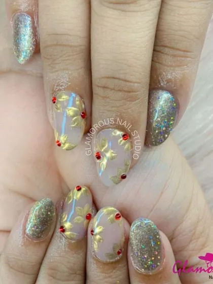 Golden leaves and a touch of sparkle. This elegant design features a sheer nude base with gold-leaf floral patterns, accented with red gems and full-coverage glitter nails.