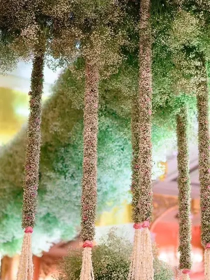 A ceiling of baby's breath creates a cloud-like effect. This installation features thick columns of flowers hanging from the ceiling, adding a magical and ethereal quality to the event space.
