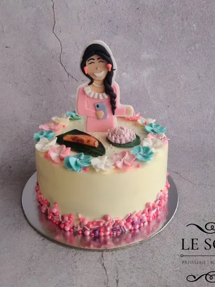 A cake celebrating all of Mansi's favorite things. This 1 kg Milk Chocolate Truffle cake is topped with a custom figurine and decorated with fondant versions of 'ela ada' and a lotus, surrounded by buttercream flowers.