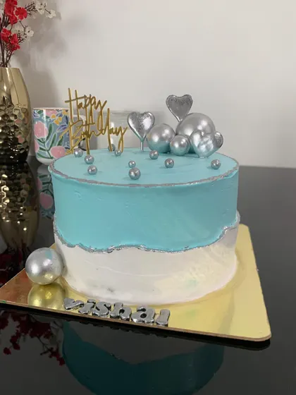 A stylish two-tone cake in teal and white with silver accents. The cake is topped with silver hearts and chocolate balls for a modern look.