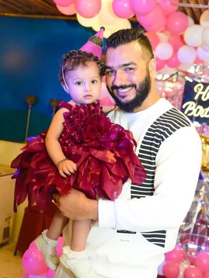 A father holds his adorable daughter at her birthday party. Her unique floral dress is simply stunning.