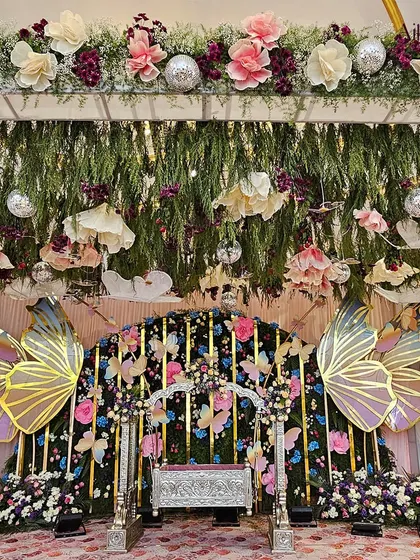 A detailed shot of the whimsical butterfly naming ceremony stage. The hanging paper flowers, clouds, and disco balls add layers of texture and fun to the overall design.