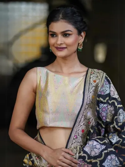 A model wearing the pale gold brocade blouse, showing its flattering fit and how it complements a dark, intricately patterned saree.