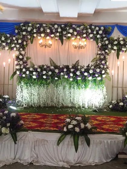 A close-up of the stage for a Half Saree function, featuring a heart-shaped floral design in white and purple with cascading flowers.