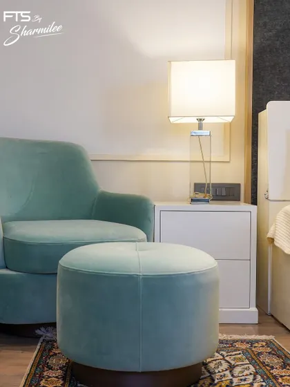 A cozy reading corner in a bedroom, featuring a custom-made mint green velvet armchair and a matching tufted ottoman. This little nook is designed to be a perfect spot to unwind with a book.