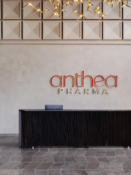 A focused view of the main reception desk in the entrance lobby. The desk is crafted from teakwood with dark wenge-stained beading, contrasting with the company's logo and the raw textures of the surrounding space.