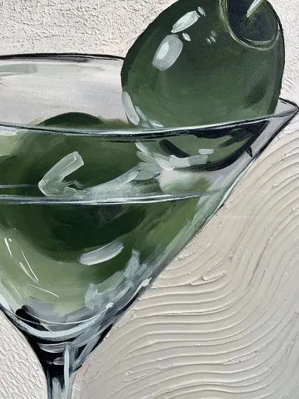 A close-up on the martini glass, highlighting the shine on the olives and the subtle texture of the background.