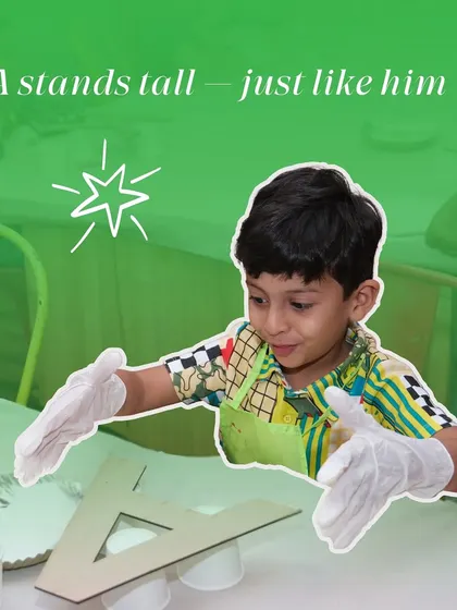A young boy proudly presents the large letter 'A' he is about to paint, standing tall just like his creation.