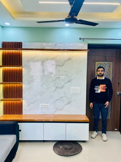 Here I am in front of a newly installed TV cabinet. The design uses a white marble-look panel with wooden fluting and a white and wood console.