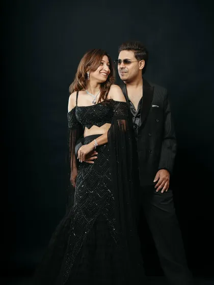 An elegant studio portrait capturing a quiet, loving gaze between the couple. The sophisticated black attire and the simple black background put the focus entirely on their connection, resulting in a classic and romantic photograph.