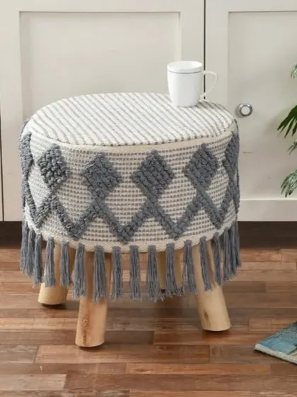 A grey and white diamond-patterned boho stool with tassels. The geometric design adds a modern touch to its bohemian feel.