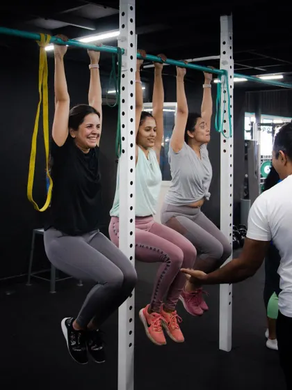 Training is better with friends. Three of our members work on their pull-up strength, using the bar for dead hangs while a coach guides them. This shows how we use partner and group work to make training social and effective.