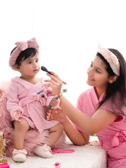 A playful spa day for mother and daughter. Dressed in matching pink robes, they share a fun moment with makeup brushes, creating a unique and adorable memory.