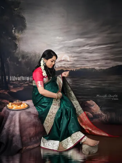 A quiet moment of reflection. Seated against a painted landscape, the mom-to-be in her saree looks down, creating a serene and contemplative portrait.
