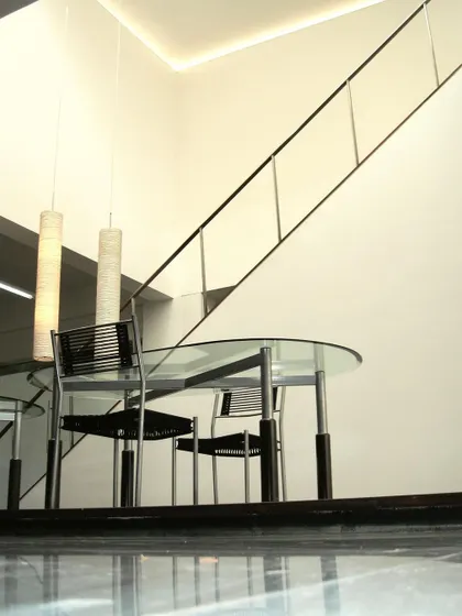 A meeting area at the Zanav Home Studio, seen from a low angle that emphasizes the polished floor and the light, transparent quality of the furniture and railing. The space is designed to feel open and uncluttered.
