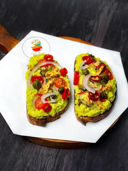A close-up of the avocado toast, showcasing the colorful and fresh toppings. The dark, rustic background makes the dish feel artisanal and wholesome.