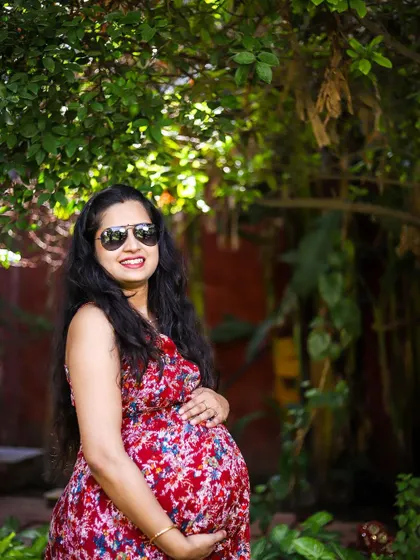 A confident and happy solo maternity portrait. The combination of the vibrant red floral dress, sunglasses, and the natural setting gives this photo a relaxed and stylish feel, perfect for capturing the personality of the mother-to-be.