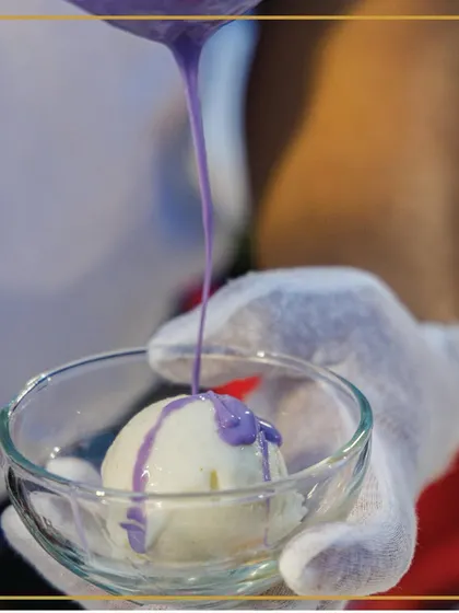 Scooping up smiles, one scoop at a time. A chef pours a vibrant purple sauce over a scoop of ice cream, creating a visually appealing and tasty treat.