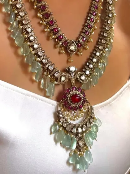 A layered necklace set with a long Rani Haar and a matching choker. This design is perfect for brides, featuring rich green or red stones and intricate detailing for a complete and opulent look.