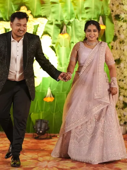 A happy couple walking hand-in-hand at their wedding event. The bride's pink lehenga and the groom's sparkling blazer are a perfect match.