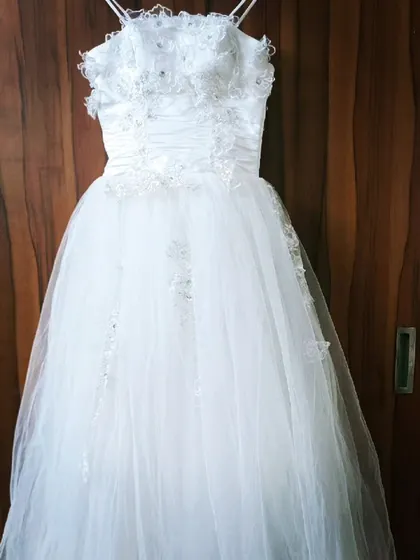 A full-length shot of the white corset gown on a hanger. You can see the delicate beading on the bodice and the soft, flowing tulle skirt.
