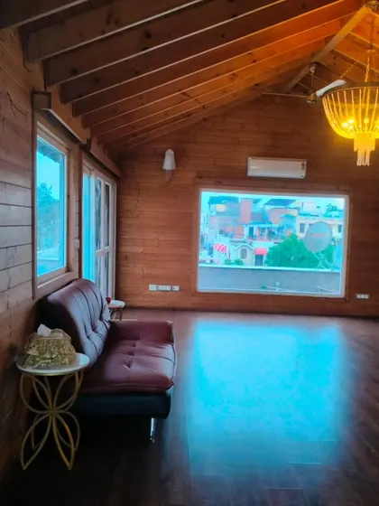 The interior of a rustic wooden cottage built on a terrace in New Friends Colony. The room is paneled with natural wood, creating a warm and cozy cabin-like feel.