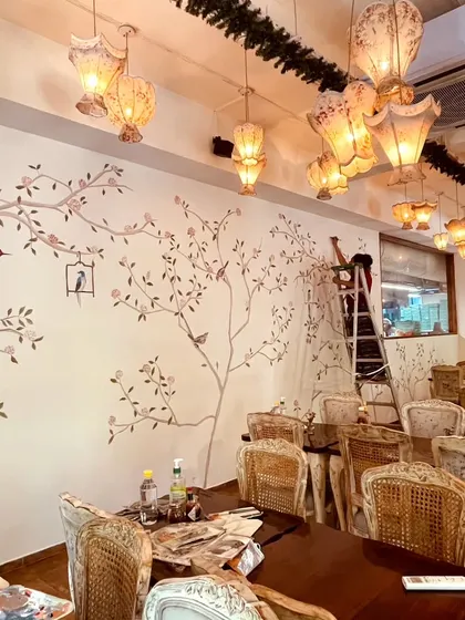 A wide shot of the Cafe Wink dining room during the painting process. The mural is designed to complement the vintage chairs and lighting fixtures.