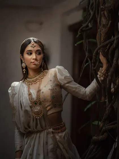 A portrait of a bride, her face framed by the roots of a tree. This artistic composition blends her traditional beauty with the raw, natural elements of the earth.