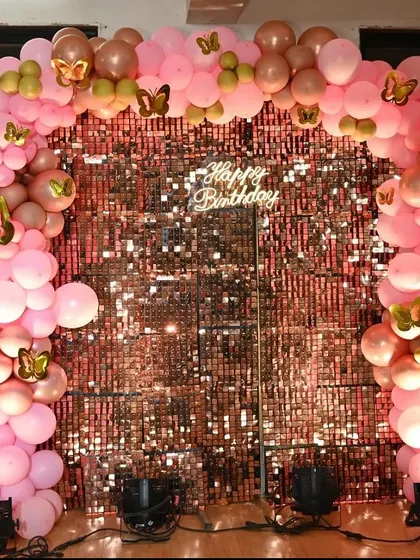A beautiful birthday backdrop with a rose gold shimmer wall. The wall is framed by a pink and rose gold balloon arch with butterfly accents.