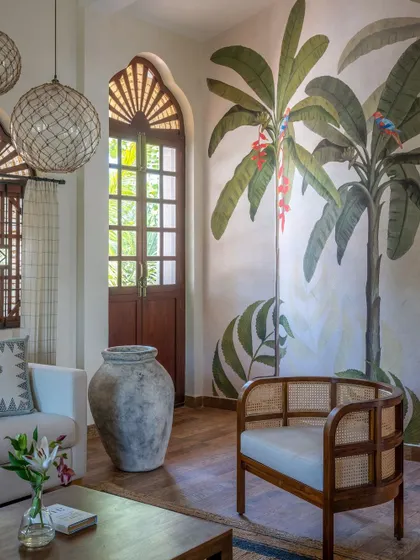 A stunning hand-painted mural of banana trees brings the tropical outdoors inside in this Goan holiday home. The cane armchair and large urn add to the earthy, relaxed aesthetic.