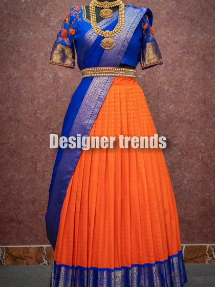 A vibrant half saree combining a bright orange skirt with a royal blue blouse and dupatta, showcasing a bold and beautiful color combination.