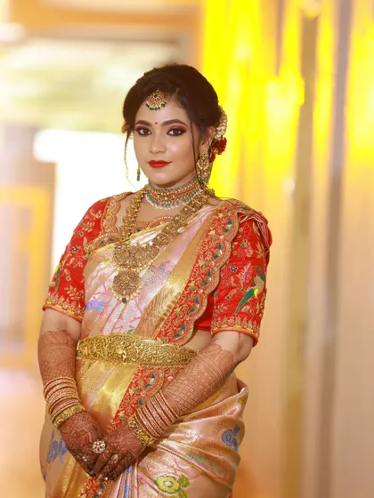 This bride wears a classic soft peach-toned silk saree with a beautiful handmade border. I designed a striking red blouse, intricately embroidered with flora and fauna motifs, to complement the saree perfectly.