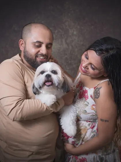 An expecting couple lovingly holds their adorable dog during their studio maternity session. Their smiles and gentle hold on their pet show the joy that animals bring to a family.