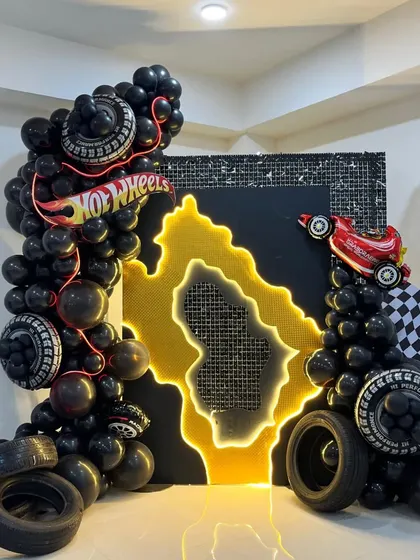 A stylish Hot Wheels themed photo corner with a black and gold color scheme, featuring a neon-lit map and balloon garlands with tire accents.
