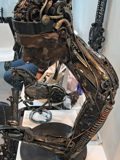 A close-up of the metal sculpture of a person reading, highlighting the intricate assembly of gears, springs, and plates.