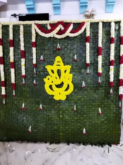 A traditional backdrop for a Ganesha pooja, made from woven green leaves and featuring a Ganesha motif made of yellow flowers.