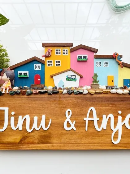 A clean, top-down view of the colorful neighborhood nameplate. You can see the detail in the hand-painted houses, the tiny birds, and the couple figurine that makes this piece so special.