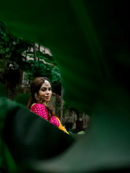 A creative portrait of the bride peeking through lush green leaves during her Haldi ceremony. This playful and unique shot adds an artistic touch to the gallery.