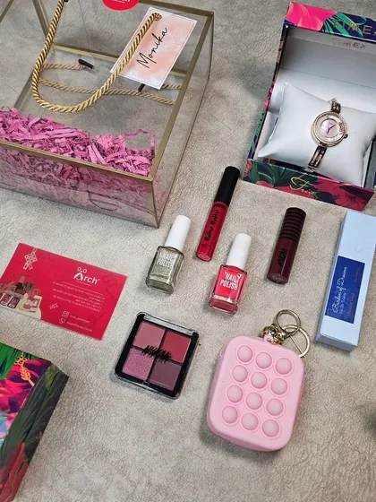 The contents of a stylish Rakhi hamper for a sister. This gift includes a watch, makeup, perfume, and a pop-it keychain, all ready to be packed in our signature transparent box.
