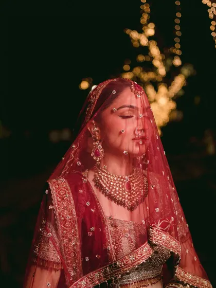 An artistic portrait with the bride's face partially obscured by her red veil. The dramatic lighting and color create a powerful and emotive image.