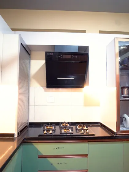 A compact L-shaped kitchen featuring mint green cabinets and a black countertop. The design includes a rolling shutter unit for appliances, keeping the counter space free and uncluttered.