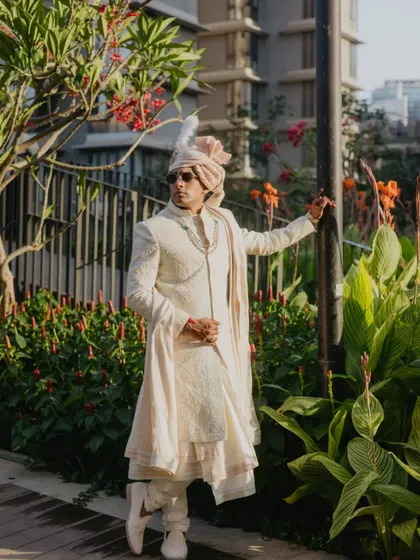 A stylish groom portrait captured in natural light. The groom's confident pose and traditional attire are complemented by the lush green surroundings, creating a modern yet timeless image.