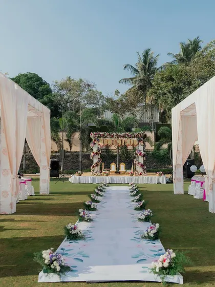 A beautiful outdoor wedding aisle, featuring a custom-printed runner with a delicate leaf pattern. The aisle leads to a floral mandap, all set up on a lush green lawn for a fresh and modern ceremony.