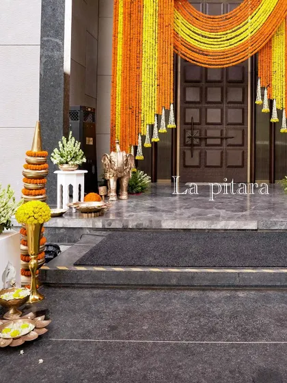 The entrance doorway was draped with cascading curtains of yellow and orange marigolds. This traditional floral decor, known as a toran, adds a festive and auspicious welcome to any Indian event.